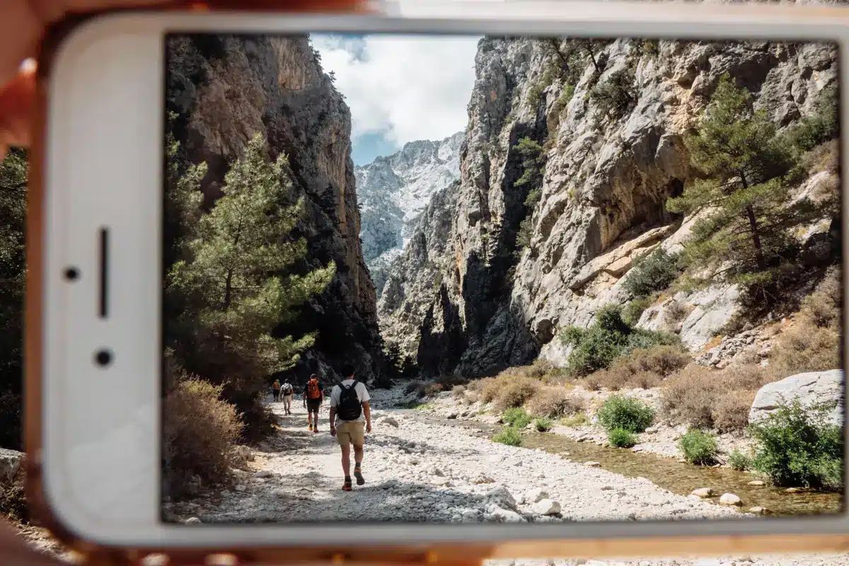 Randonneurs marchant dans un canyon, capturés à travers l'écran d'un smartphone, montagnes en arrière-plan.