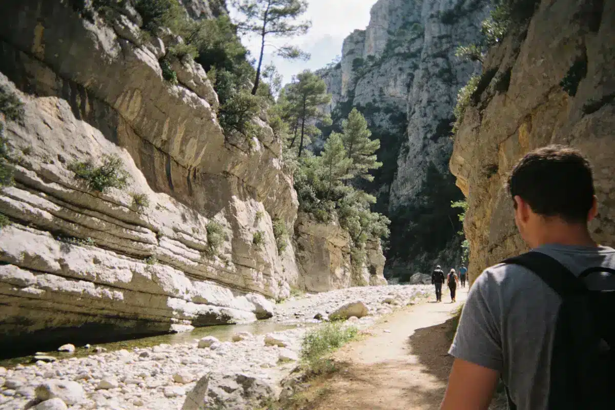 Personnes marchant dans un canyon étroit, entourées de falaises rocheuses et arbres, chemin de randonnée ensoleillé.