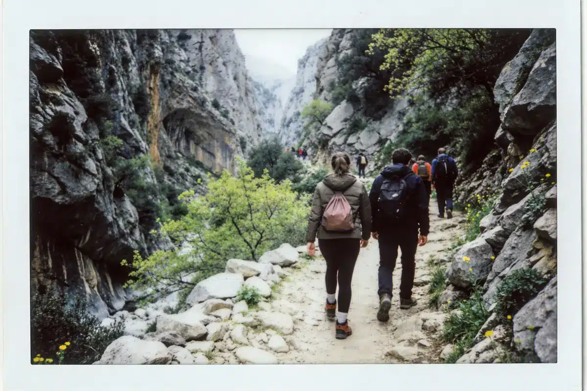 Personnes randonnant dans un canyon rocheux, entouré de falaises et végétation, par temps nuageux.