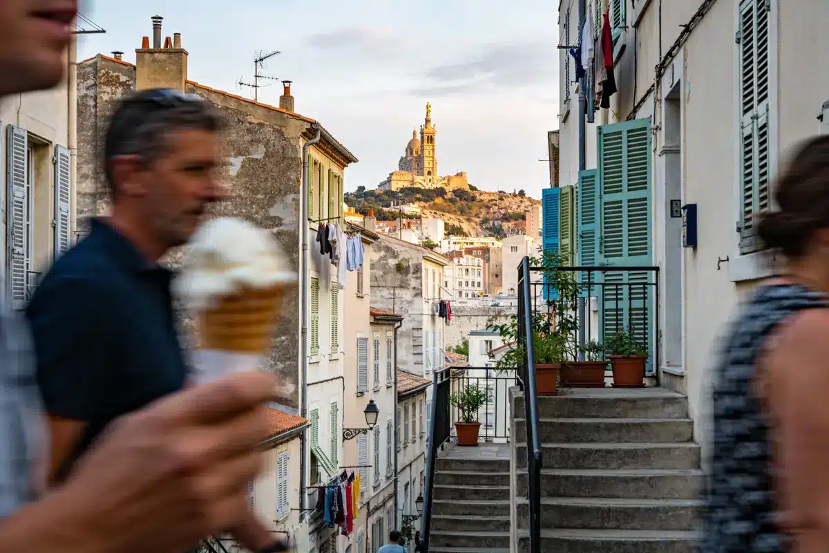 Escalier de rue à Marseille, vue basilique Notre-Dame de la Garde, homme avec glace au premier plan.