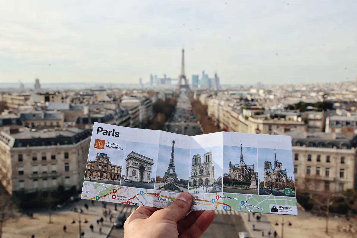 Carte touristique de Paris tenue par une main, vue sur la ville et la Tour Eiffel en arrière-plan.
