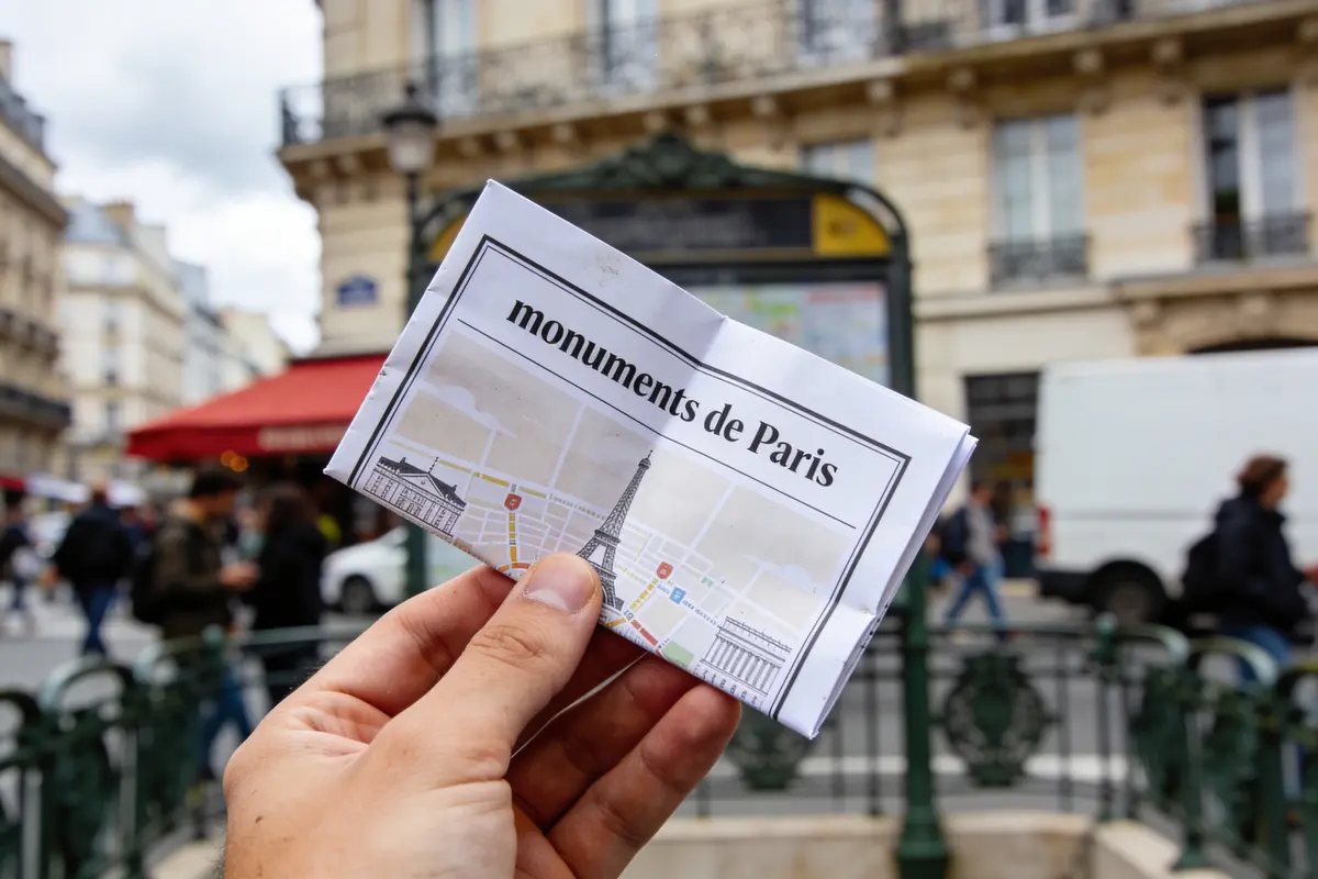 Personne tenant carte des monuments de Paris, rue animée en arrière-plan.
