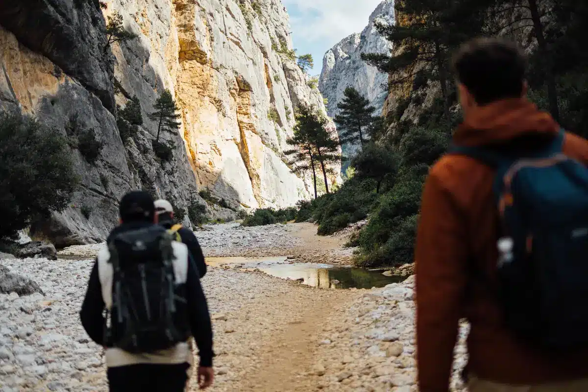 Randonnée dans un canyon rocheux avec sentier de pierres, arbres et randonneurs portant des sacs à dos.