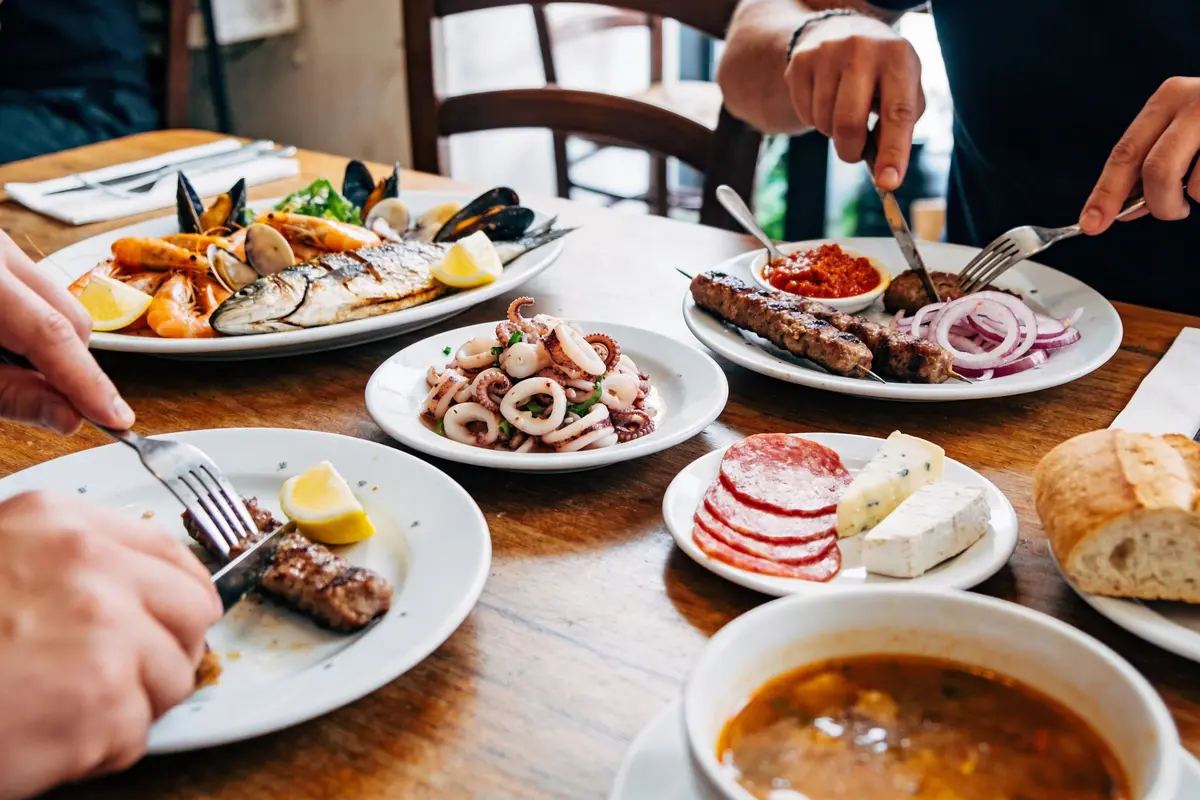 Assiette de fruits de mer variés, viande grillée avec oignons, charcuterie, fromage, soupe, pain sur table en bois.