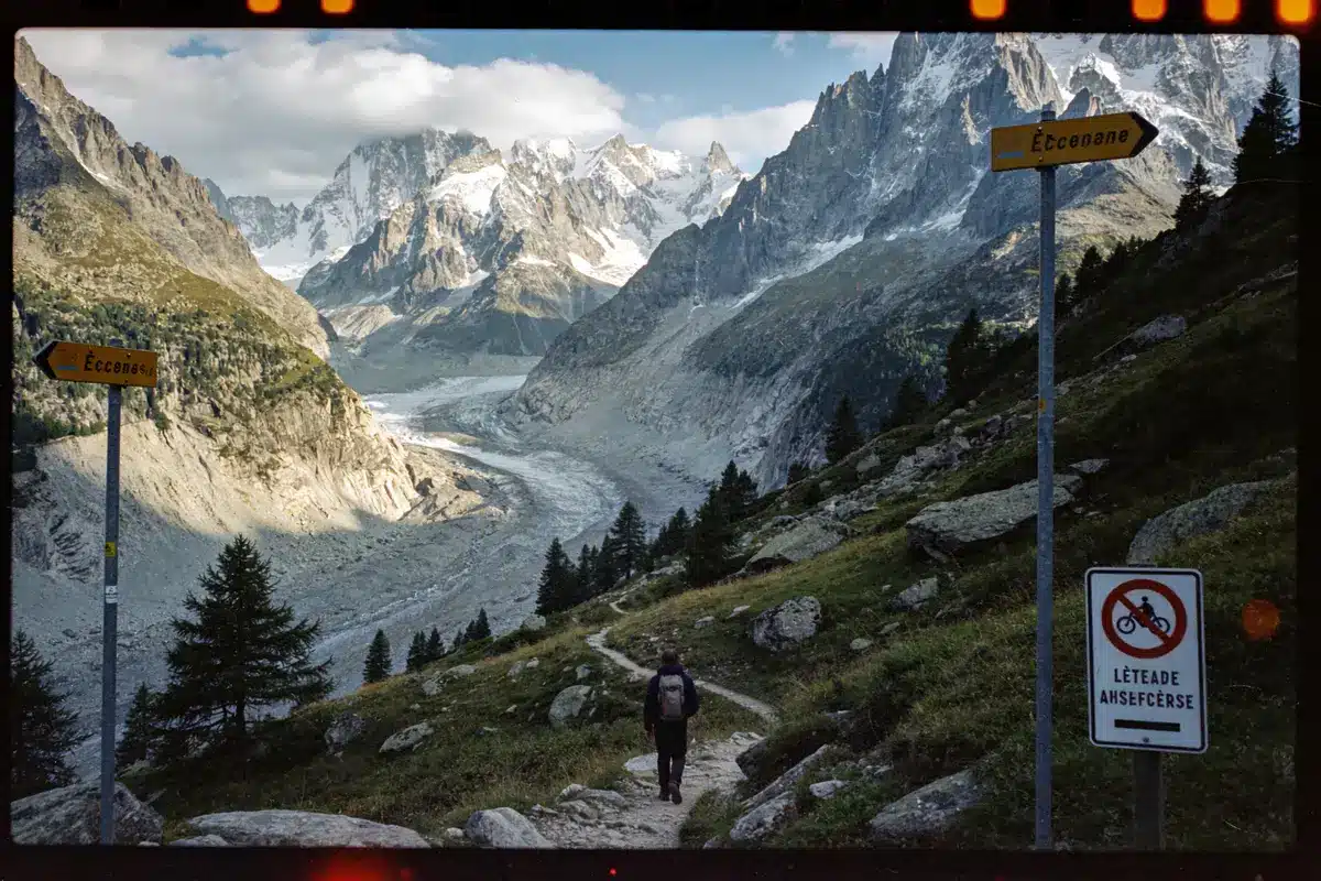 Une personne marche sur un sentier de montagne avec vue panoramique sur les sommets enneigés.