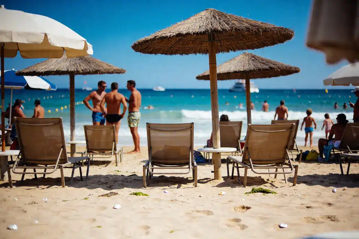 Chaises longues et parasols sur plage ensoleillée, personnes profitant de la mer en arrière-plan.