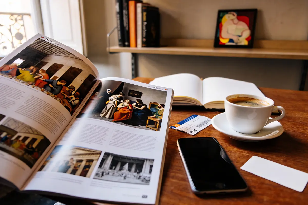 Personne tenant une carte près d'une fenêtre, smartphone et livres sur la table.