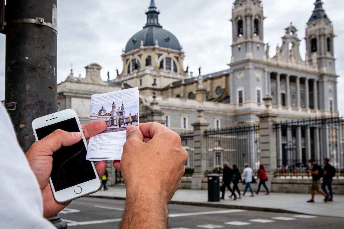 Une personne lit un magazine de voyage, avec un téléphone et cartes sur la table.