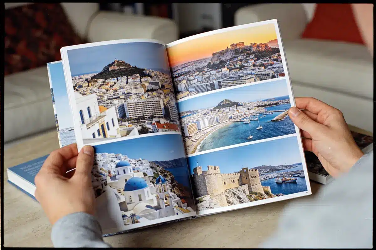 Livre ouvert avec photos de paysages urbains et côtiers, montrant des bâtiments et mer. Persone tenant le livre.