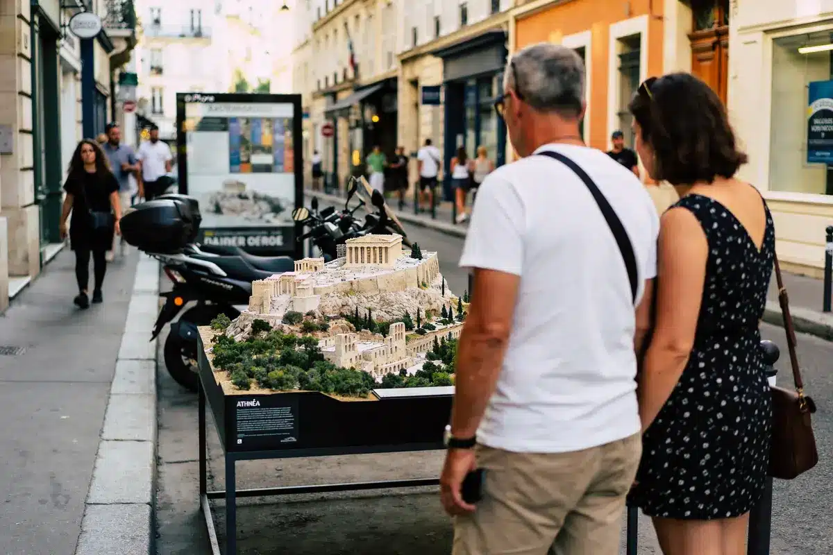 Deux personnes regardant une maquette de l'Acropole dans une rue animée de la ville.